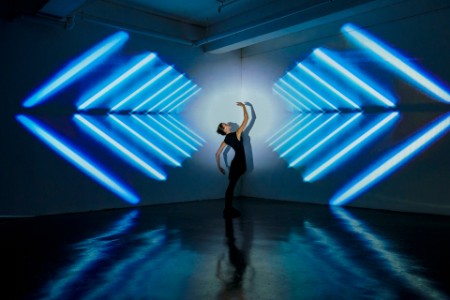 Girl dancing in a studio with graphic patterns projected onto wall behind her