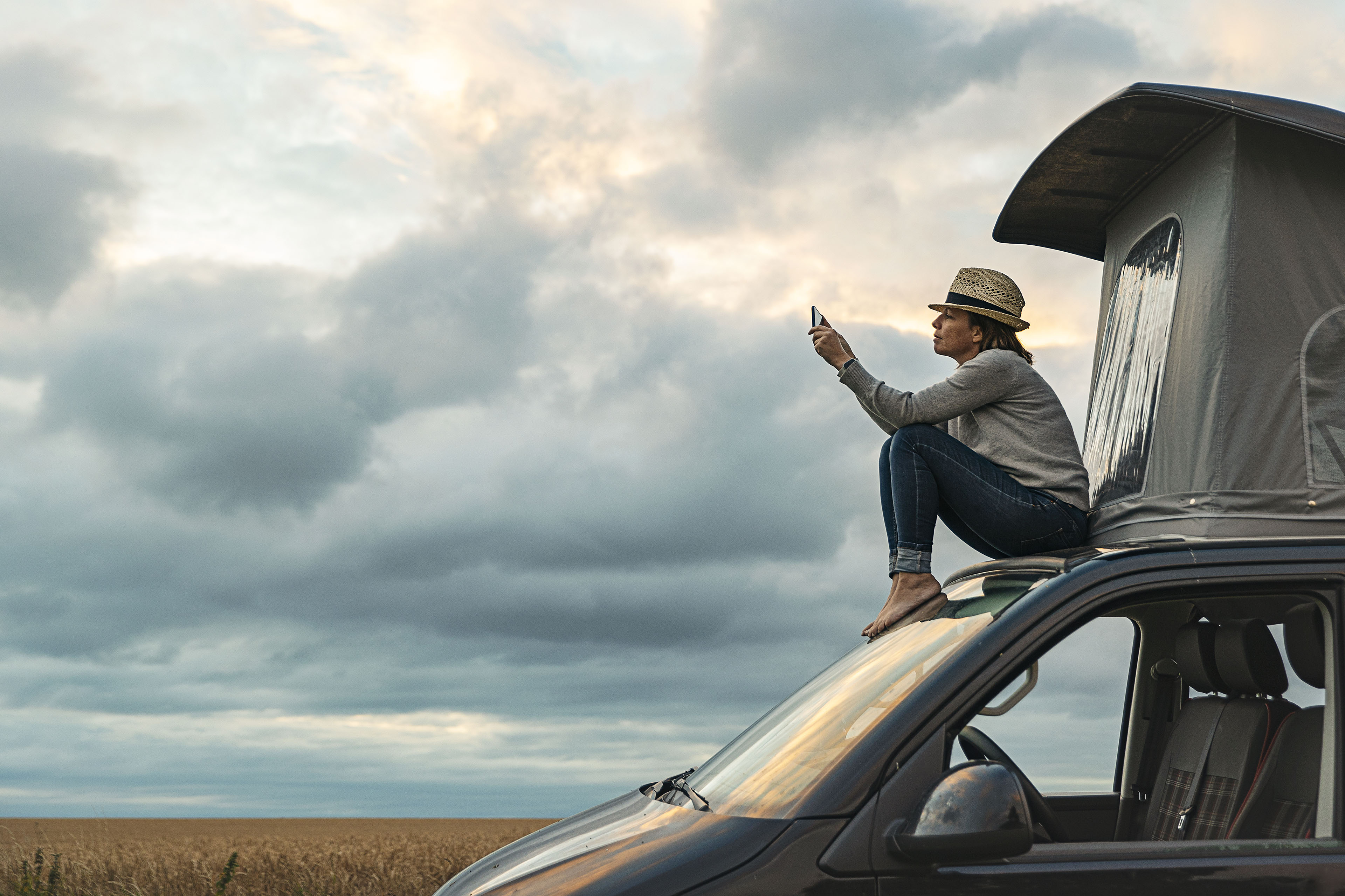Woman taking a photo whilst sitting on roof of camper at sunset Child walking on footpath